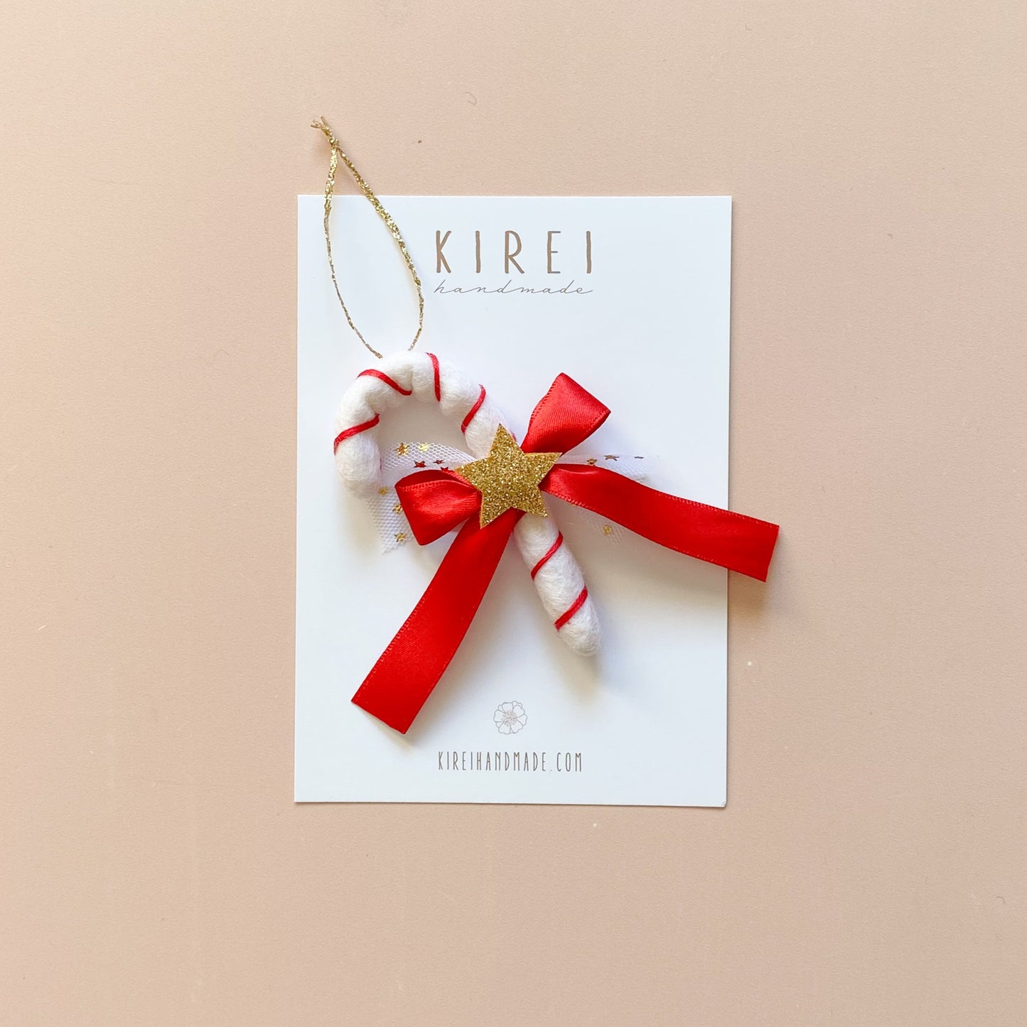 A red candy cane Christmas ornament attached to a gold glitter string