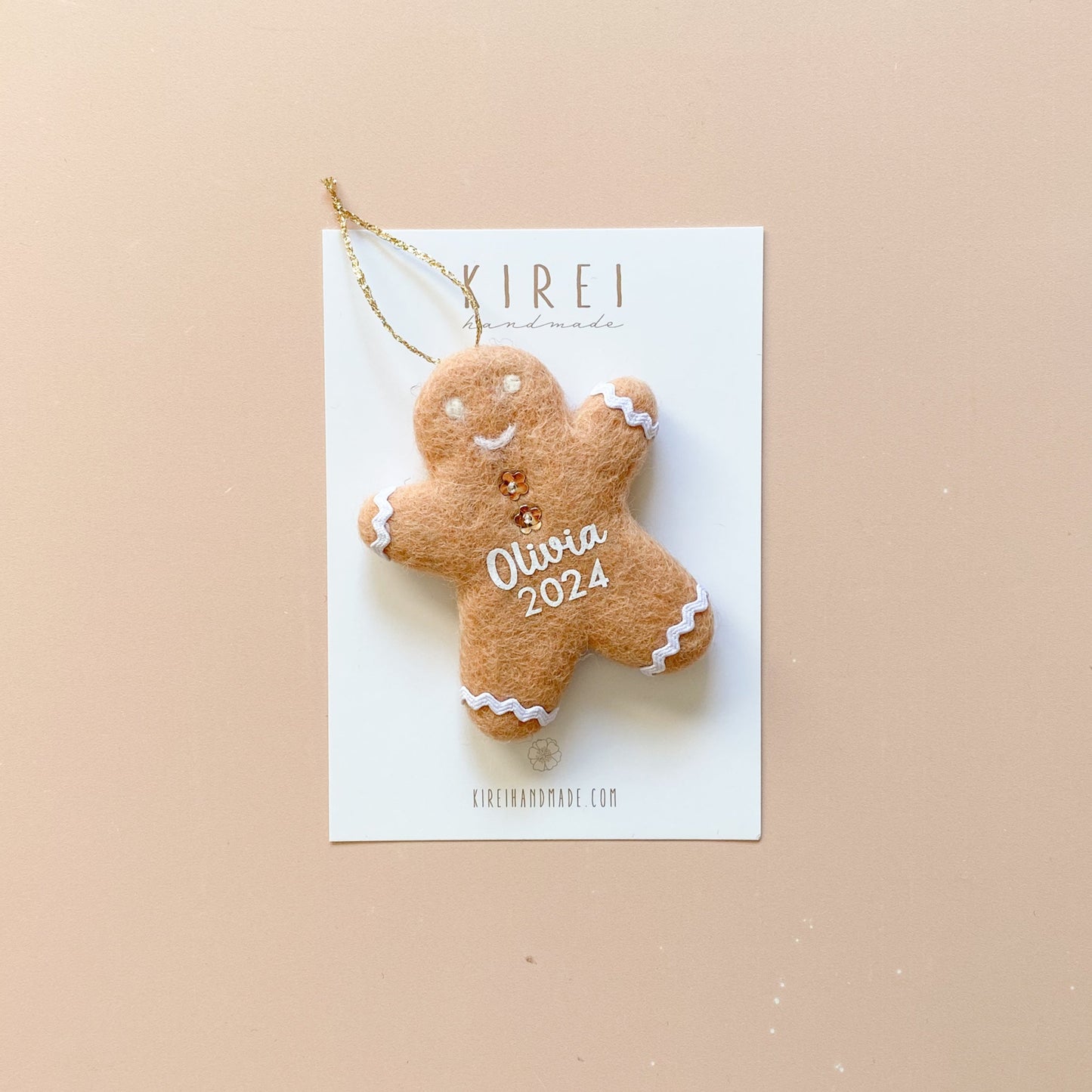 A felt Christmas ornament in the shape of a gingerbread man with daisy buttons, beige in color, with a gold glitter string attached for hanging