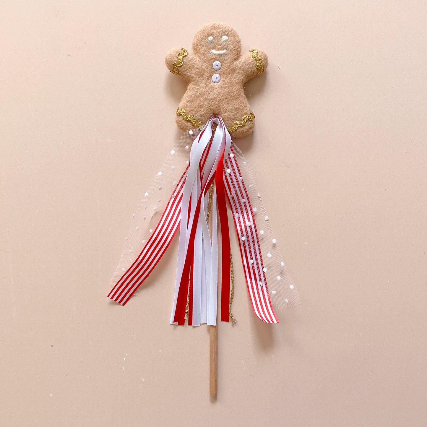 A decorative gingerbread man wand with a round buttons pattern and a ribbon tassel on a wooden stick, designed for Christmas decoration.