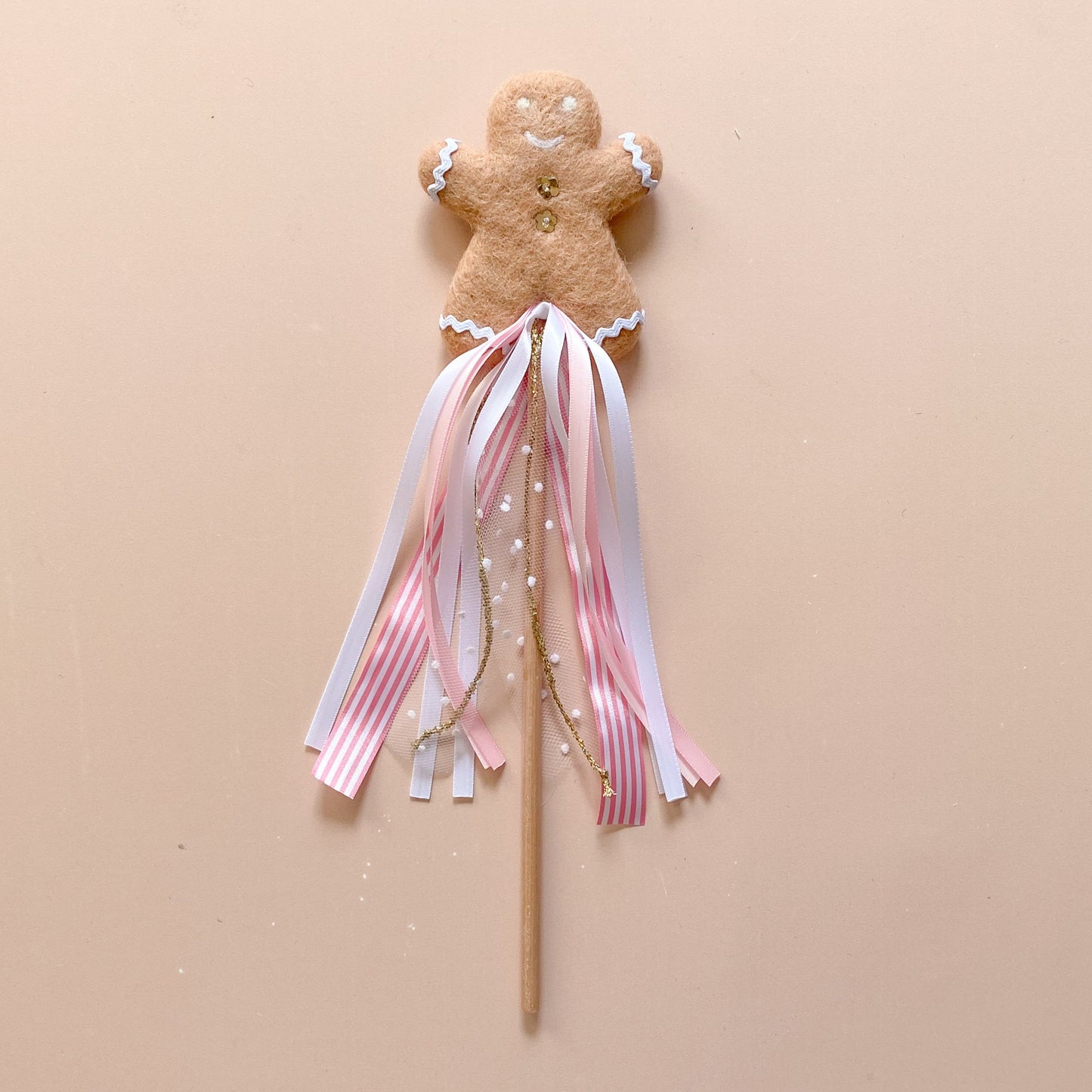A decorative Christmas wand featuring a gingerbread man shape with daisy buttons and a ribbon tassel on a wooden stick