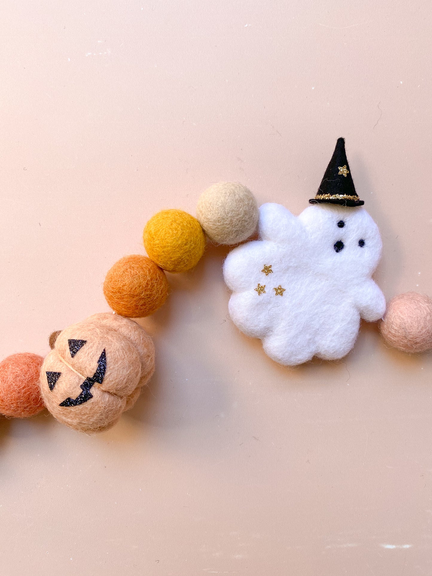 Decorative Halloween garland with felt balls, ghost with witch hat, jack o lantern pumpkin in fall colours