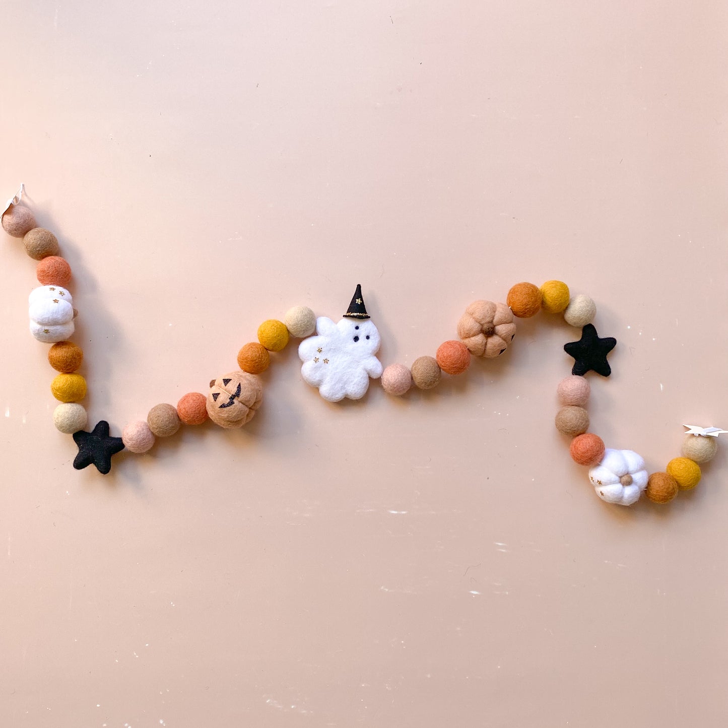 Decorative Halloween garland with felt balls, ghost with witch hat, jack o lantern pumpkin in fall colours