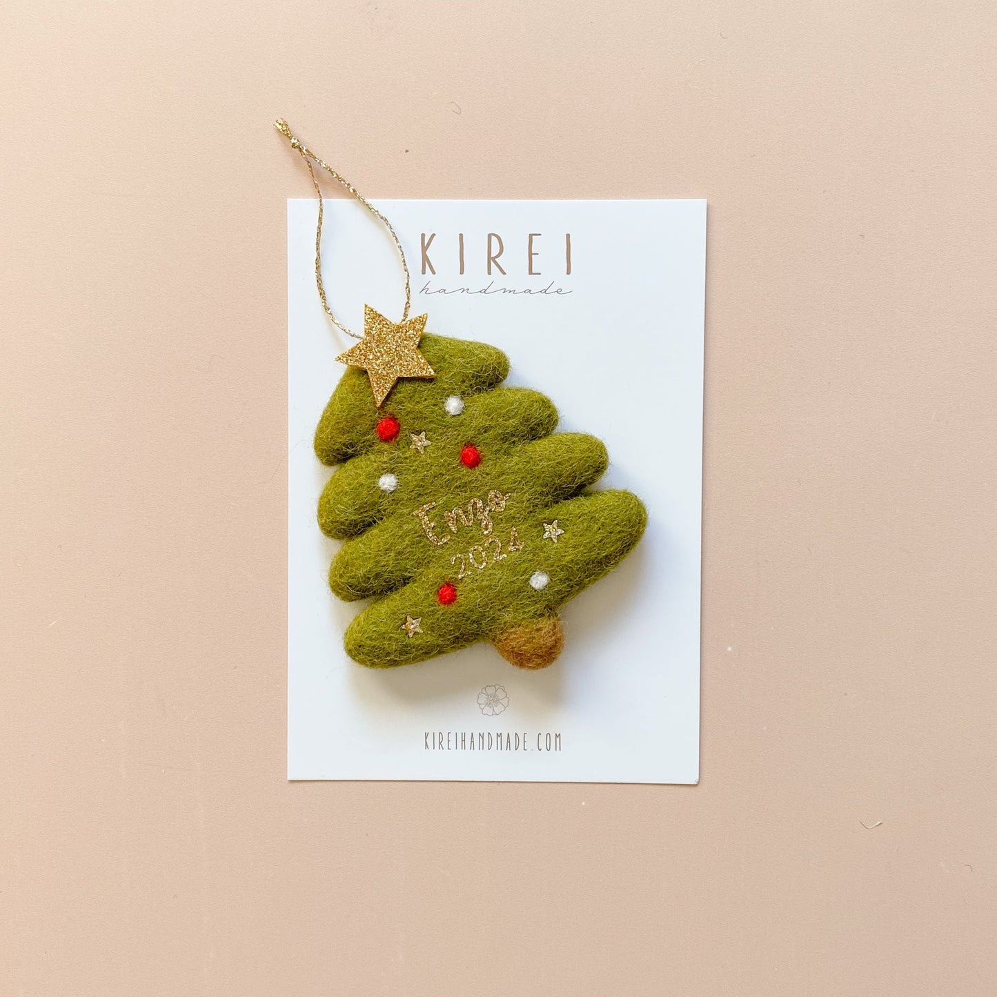 A green Christmas tree-shaped felt ornament with red and white details, attached to a gold glitter string