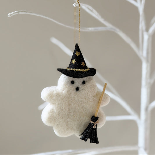 A felt ghost ornament wearing a black pointed hat with gold stars and holding a broom