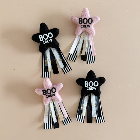 star-shaped badge with 'BOO CREW' text in black and pink with a ribbon tail featuring black and white stripes and subtle gold glitter.